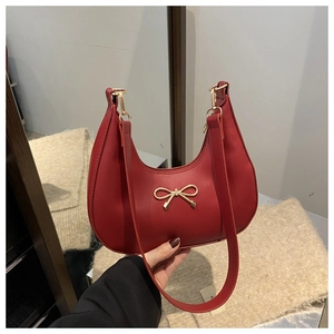 Close-up of a vintage red crescent hobo bag featuring a gold metal bow and smooth leather