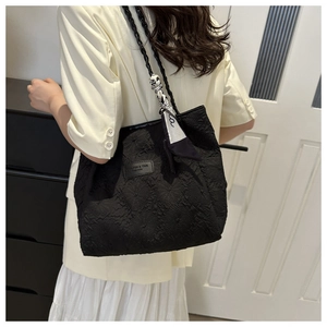 Detail of black textured tote bag featuring woven shoulder straps and a stylish scarf accent