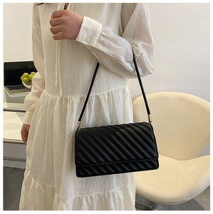 Détail d'un sac à bandoulière matelassé noir avec détails dorés et robe blanche