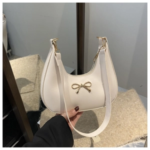 Detail of white crescent hobo bag featuring a gold metal bow and smooth leather finish