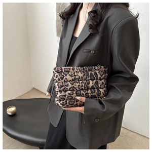 Close-up of leopard print quilted clutch bag held by a model in a grey blazer