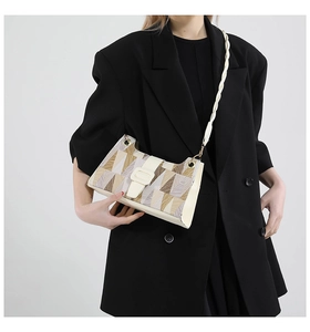 Detail of the geometric patterned flap and braided shoulder strap on a cream crossbody bag