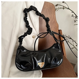 Detail of black pleated shoulder bag with metallic triangular logo and gathered strap design