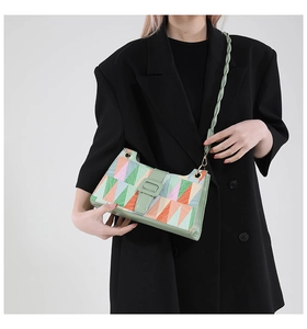 Detail of colorful geometric patchwork shoulder bag with green woven strap on model