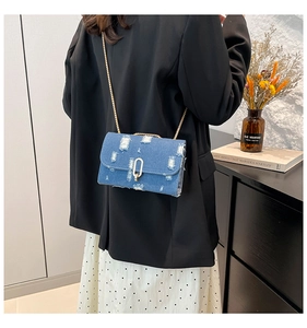 Detail of blue denim crossbody bag with distressed ripped design and gold chain strap