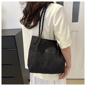 Detail of black tote bag featuring crinkled texture fabric and woven shoulder straps