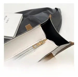 Detail of smooth gold zipper on white pebble leather tote bag with brown leather trim