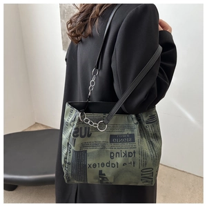 Detail of army green tote bag with newspaper print, leather strap, and silver chain