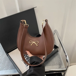 Brown faux leather crescent underarm bag with a gold bow accent and leather strap