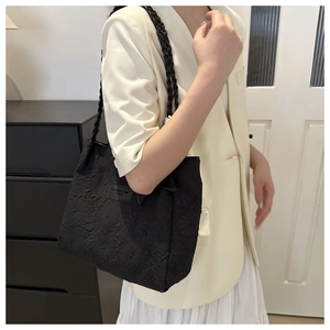 Detail of black textured tote bag featuring woven handles and leather brand label