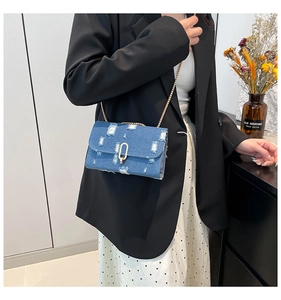 Detail of distressed denim crossbody bag with gold chain strap worn with black blazer