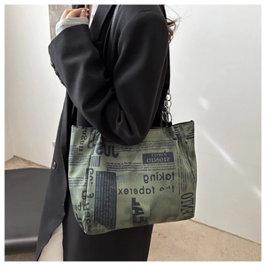 Dettaglio della borsa tote verde con stampa di giornale e catena su blazer nero
