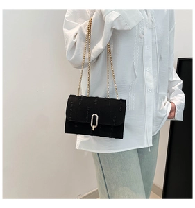 Detail of black denim bag with gold chain strap and U-shaped metal buckle closure