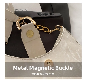 Detail of a beige leather shoulder bag featuring a gold magnetic clasp and metal chain strap