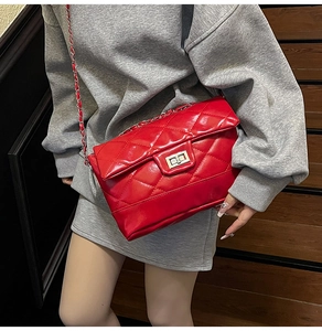 Detail of red quilted crossbody bag featuring silver chain strap and metal swivel lock