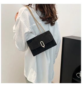 Detail of a chic black denim shoulder bag with a gold oval buckle and chain strap on a model
