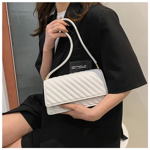Détail du sac bandoulière matelassé blanc avec ferrures dorées sur un blazer noir