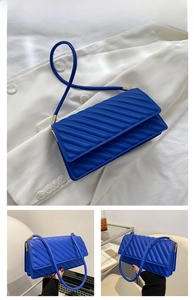 Détail du sac à bandoulière matelassé bleu avec surpiqûres sur une veste blanche chic