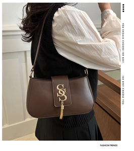 Detail of dark brown leather crescent bag featuring a gold SS logo and metal tassels