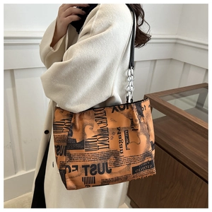 Detail of orange tote bag with black print, leather and silver chain strap