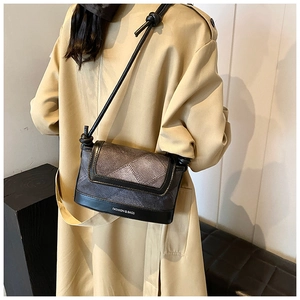 Detail of grey plaid crossbody bag with black leather trim worn on a beige trench coat