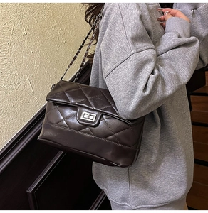 Detail of black quilted chain bag featuring silver metal turn-lock and leather strap