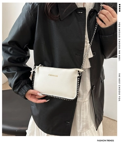 Detail of white grainy leather crossbody bag with silver studs and chain strap worn by model