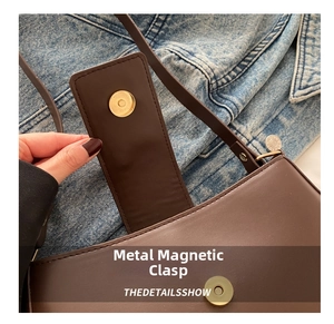 Close-up of golden magnetic buckle on brown leather crescent bag with stitching details