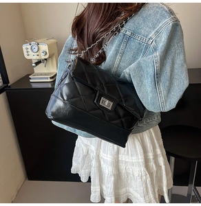 Detail of a black quilted crossbody bag with a silver twist lock and metal chain strap