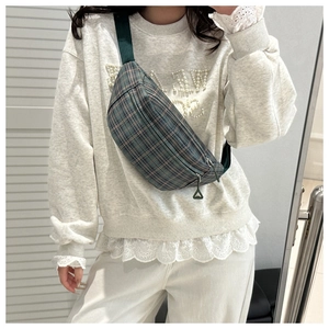Close-up of a green plaid crossbody chest bag with adjustable strap worn by a model
