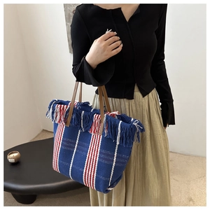 Close-up of knit tote bag featuring colorful stripes, tassel edges, and leather straps