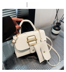 Detailed view of white pebble leather handbag with gold buckle and mini coin purse charm