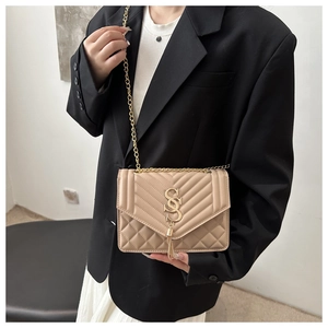 Detail of beige quilted crossbody bag with gold S-logo and metal tassel detail