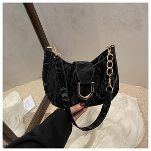Close-up of black pleated patent leather bag with gold metal chain and buckle detail
