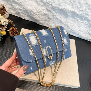 Blue denim crossbody bag with distressed detailing and gold chain strap on display