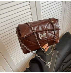 Detail of dark brown quilted crossbody bag with metal chain strap and twist-lock closure