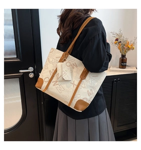 Detail view of large cream tote bag with brown leather handles and geometric letter print