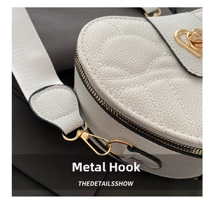 Close-up of golden metal hooks and heart-shaped lock on white litchi pattern bag