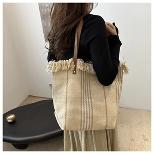 Detail of knit tote bag featuring fringe trim, vertical stripes and brown leather straps