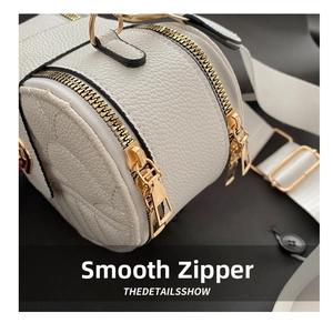 Detail of smooth gold dual zippers and litchi grain white leather texture on shoulder bag