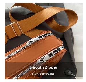 Detail view of smooth silver double zippers and wide woven strap on a brown crossbody bag