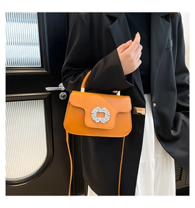 Détail du sac plissé orange avec boucle fleurie en strass et poignée de transport