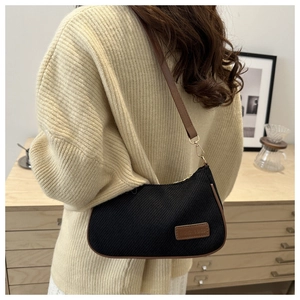 Detail of black twill crossbody bag with brown leather strap and brand logo patch