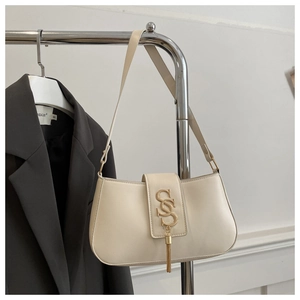 Detail of a creamy white leather baguette bag with a golden S-logo and metal fringe charm