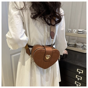 Brown leather crossbody heart bag with stitched details shown on a model in a cozy setting