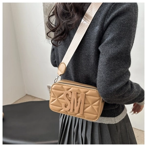Detail of khaki quilted crossbody bag with 3D SM letters and wide woven shoulder strap
