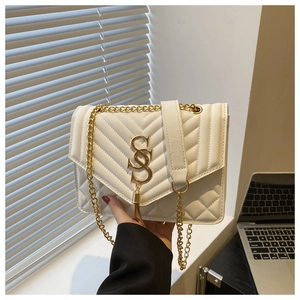 Close-up of white quilted handbag featuring gold chain and metallic tassel ornament
