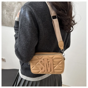 Close-up of khaki quilted small square bag with 3D SM letters and wide fabric shoulder strap