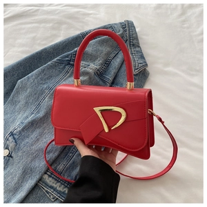 Close-up of a red leather crossbody bag with a gold D-buckle and denim jacket background