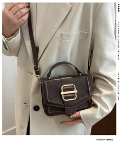 Detail of vintage dark brown leather shoulder bag with gold buckle on white blazer